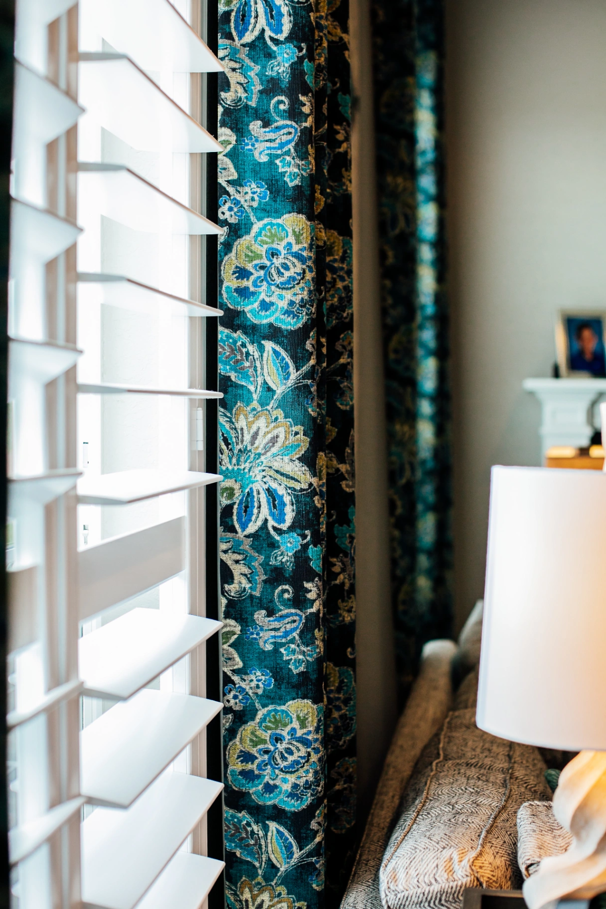 Rich teal botanical drapery layered over plantation shutters