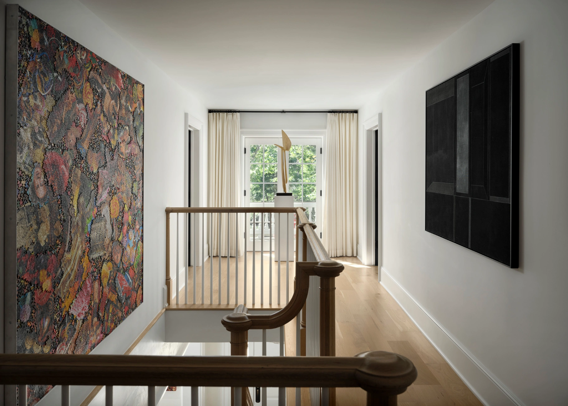 Tailored ivory floor-to-ceiling drapery panels framing French doors in a bright, art-filled modern hallway