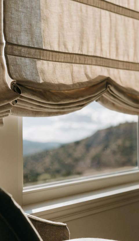 Craftsperson measuring fine linen fabric for a custom Roman shade in a workroom with folded fabric samples