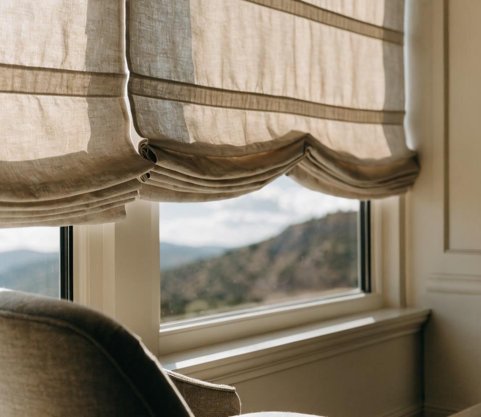 Craftsperson measuring fine linen fabric for a custom Roman shade in a workroom with folded fabric samples