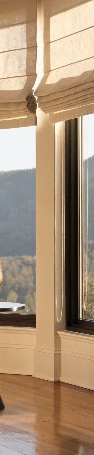 Custom flat-fold Roman shades in ivory linen dressing tall living room windows in a Denver home with mountain views