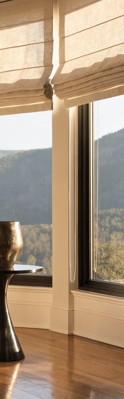Custom flat-fold Roman shades in ivory linen dressing tall living room windows in a Denver home with mountain views