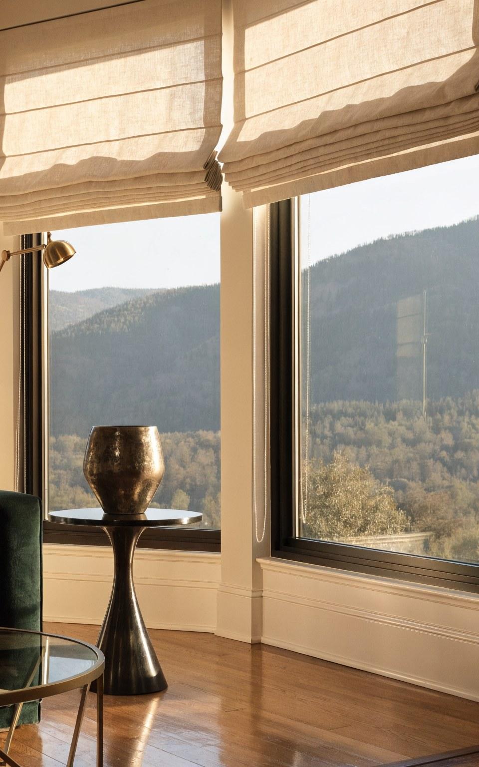 Custom flat-fold Roman shades in ivory linen dressing tall living room windows in a Denver home with mountain views