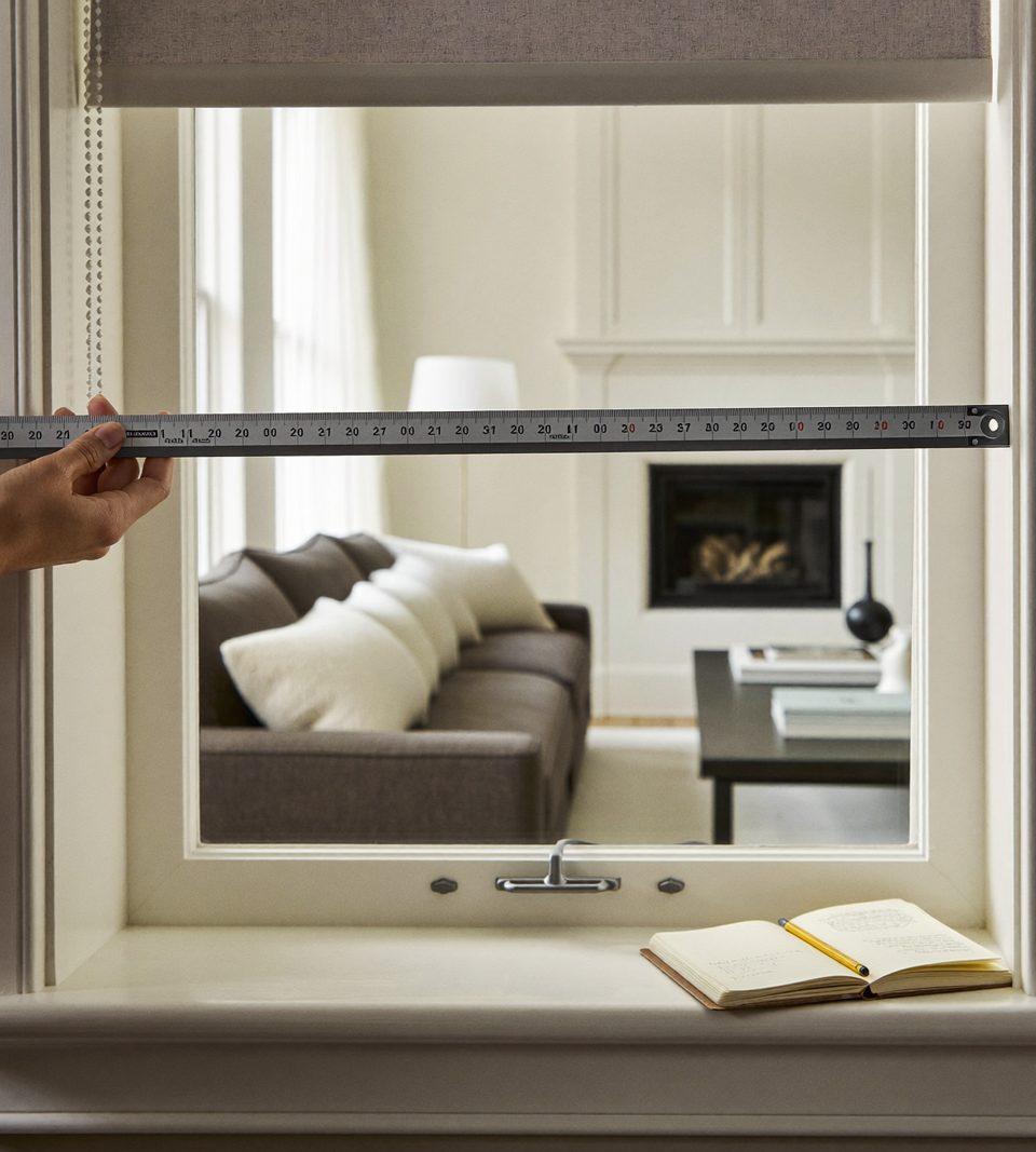 Hands measuring the inside width of a window opening with a steel tape measure for a custom shade