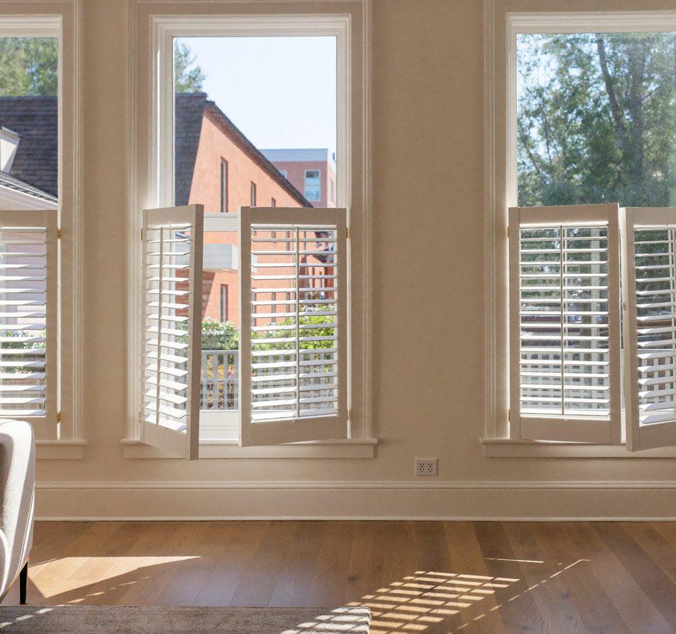 White plantation shutters with louvers tilted open on tall windows in a sunlit Denver living room with oak floors