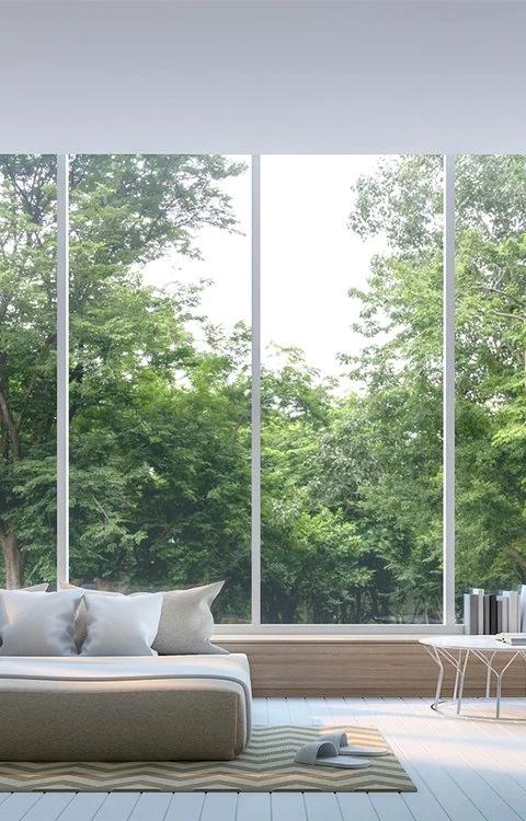 White curtains frame expansive windows behind a pale living room sofa