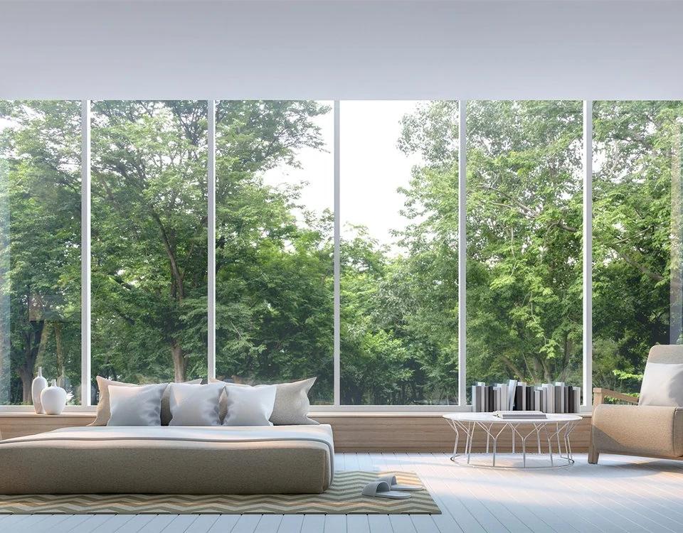 White curtains frame expansive windows behind a pale living room sofa