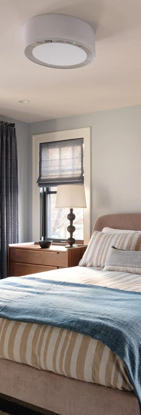 Blue bedding and dark window shades furnish a tailored bedroom