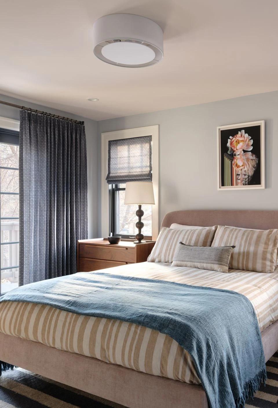 Blue bedding and dark window shades furnish a tailored bedroom