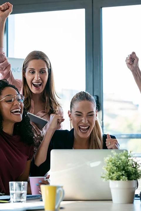 Group of women smiling together around a table with laptops