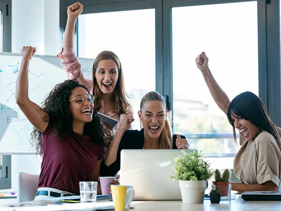 Group of women smiling together around a table with laptops