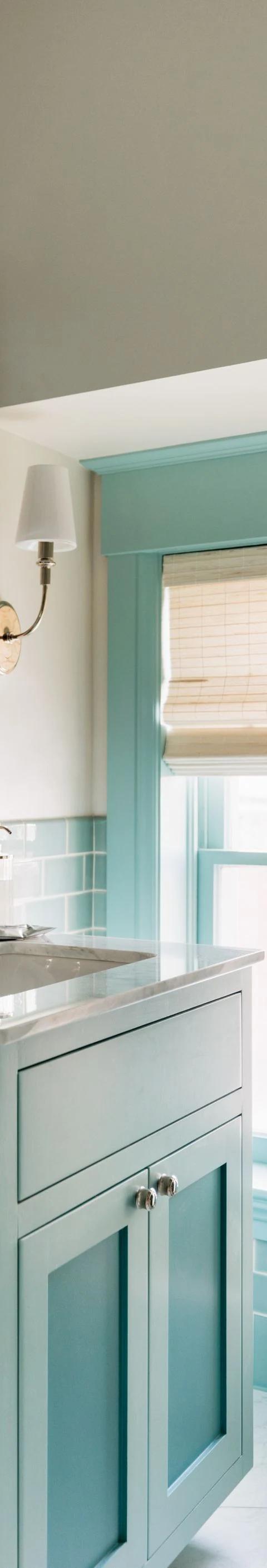 White Roman shade hangs above a turquoise bathroom vanity and mirror