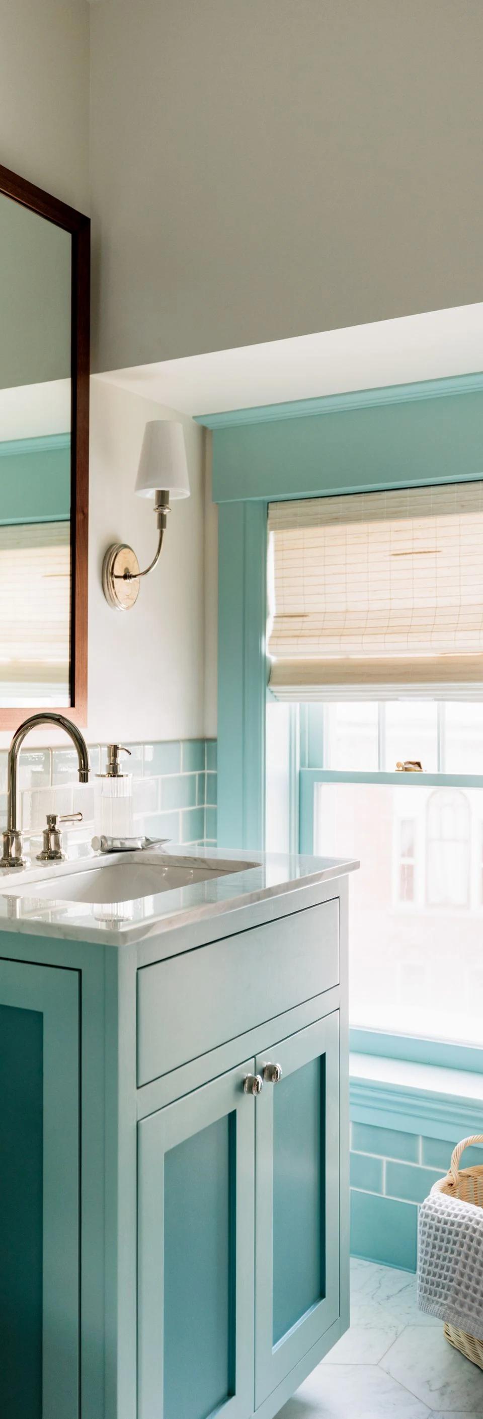 White Roman shade hangs above a turquoise bathroom vanity and mirror