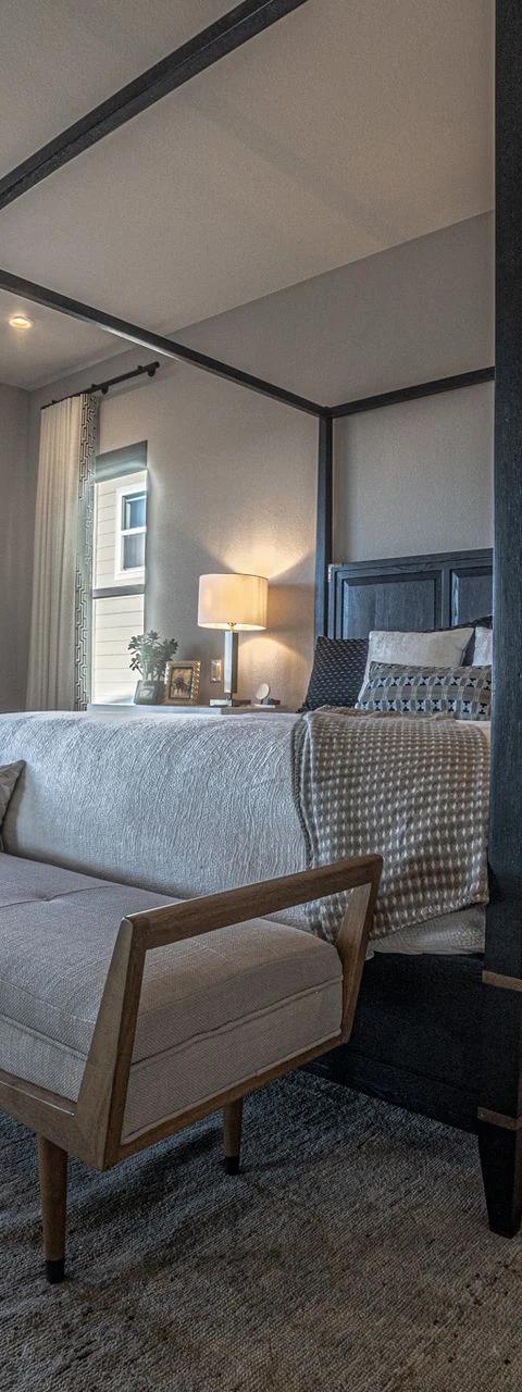 Bed beneath a dark canopy beside tall windows with distant views