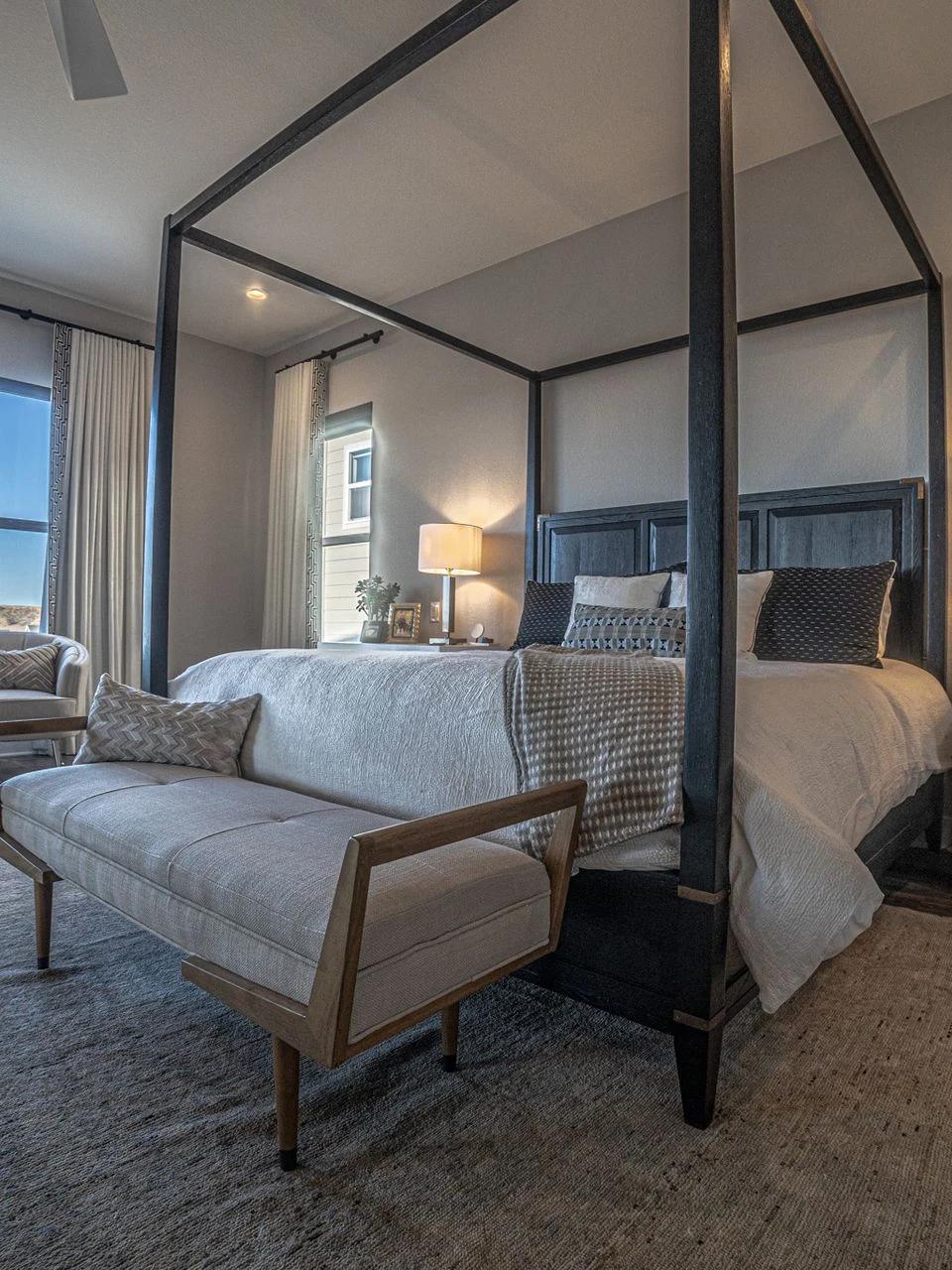 Bed beneath a dark canopy beside tall windows with distant views