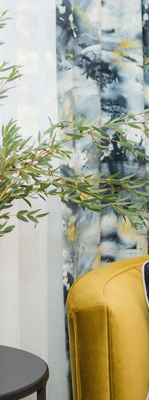 Yellow armchair beside a window with blue floral drapery panels
