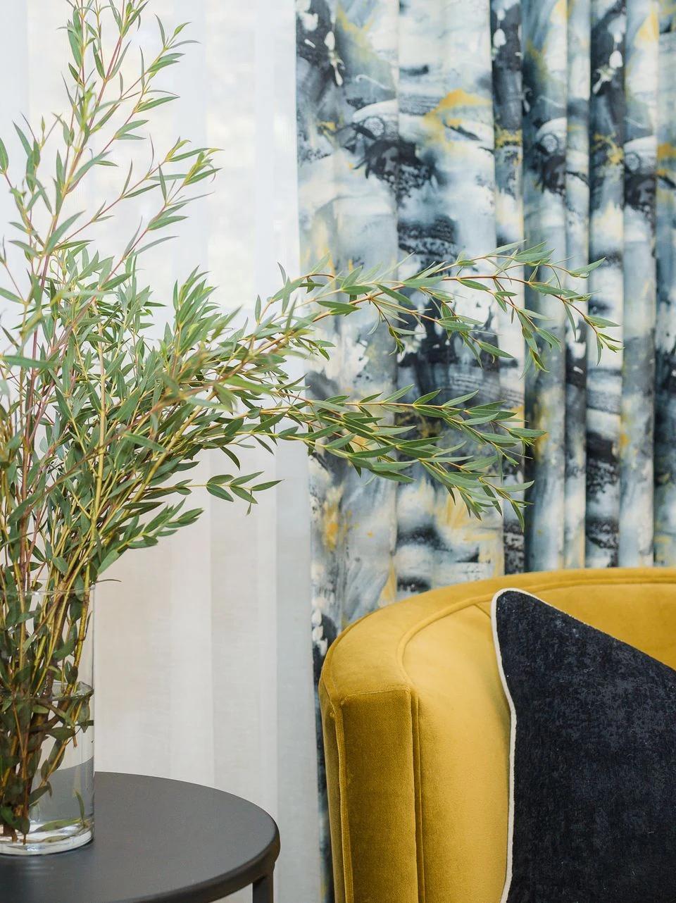Yellow armchair beside a window with blue floral drapery panels