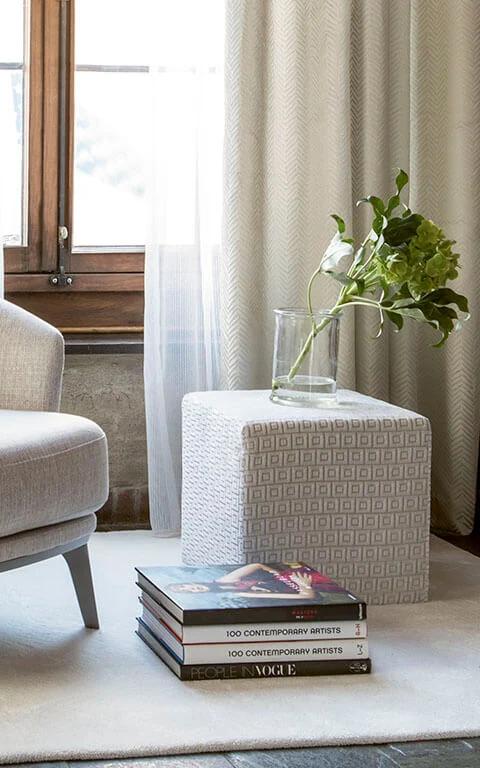 Neutral upholstered chair beside pale drapery and a small side table