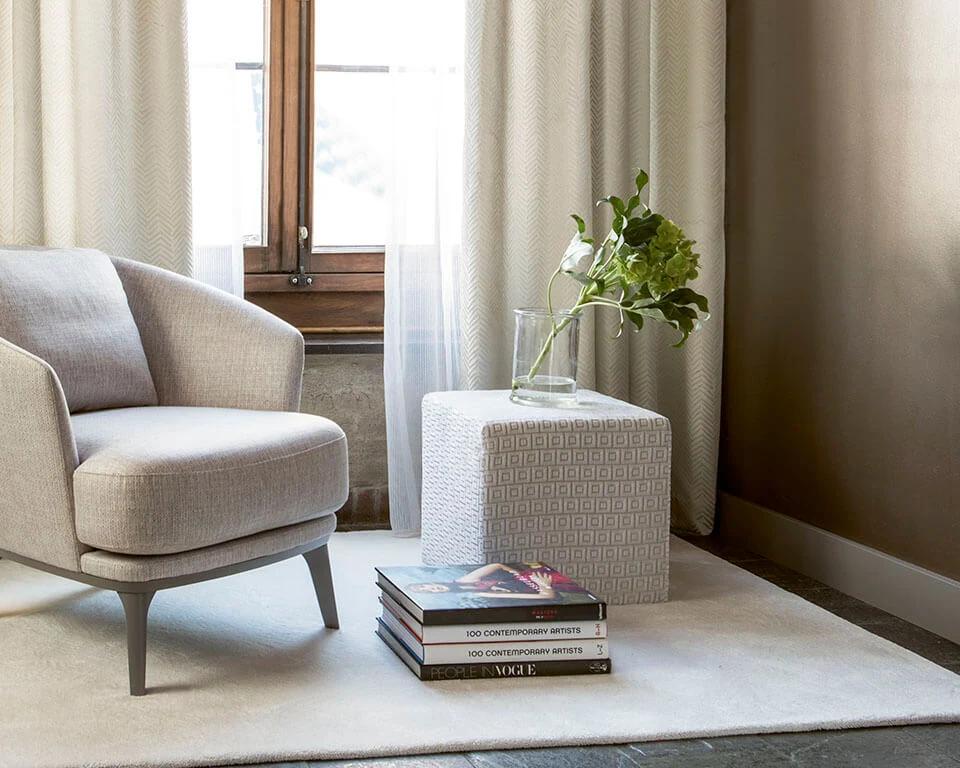 Neutral upholstered chair beside pale drapery and a small side table