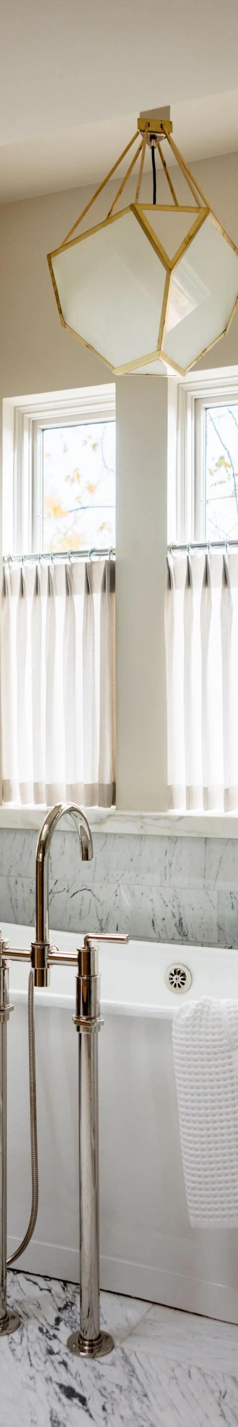 White window treatments surround a freestanding bathtub in a bright bathroom