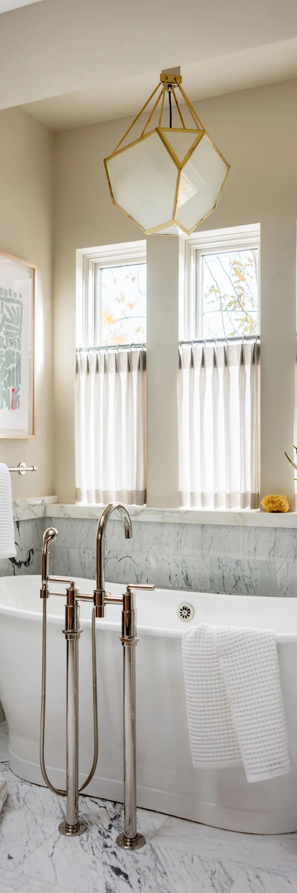White window treatments surround a freestanding bathtub in a bright bathroom