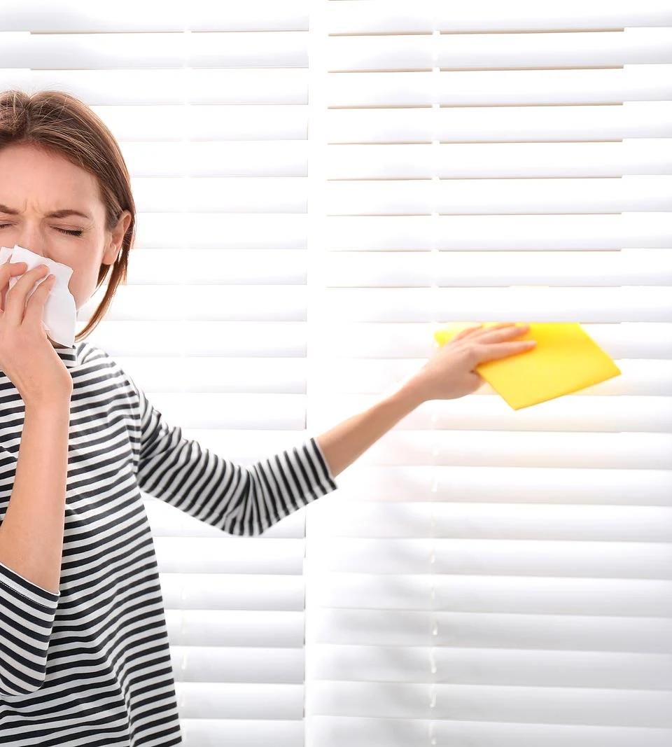 Woman cleans white horizontal blinds with a cloth beside a window