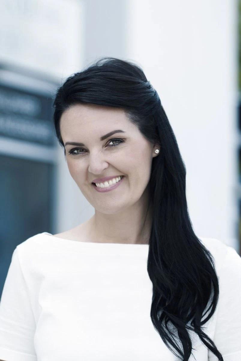 Portrait of Jessica Work smiling in a white top against a pale background