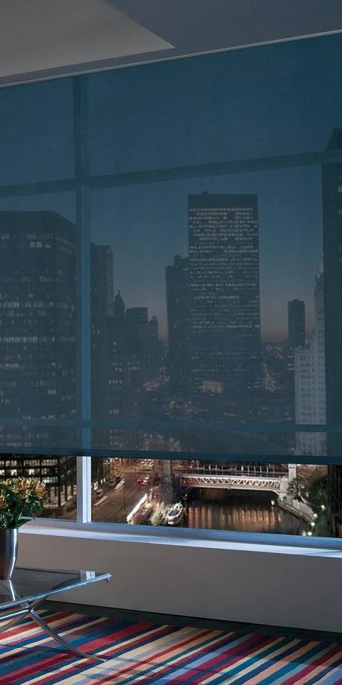 Dark solar shade covers a broad window overlooking a city skyline