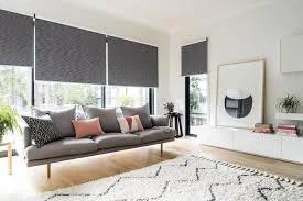 Gray roller shades cover living room windows above a sofa