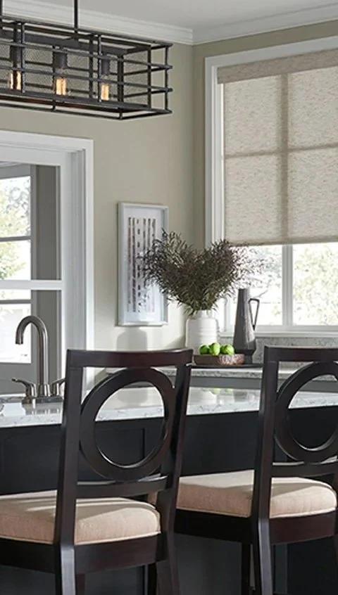 Kitchen windows with light coverings above a table and pale cabinetry