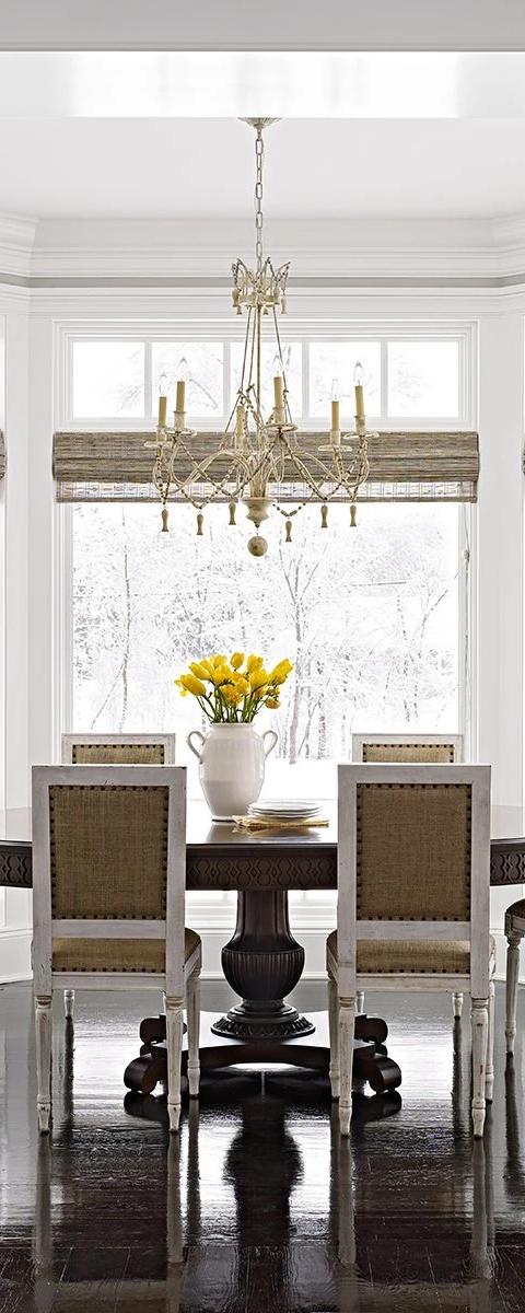 White window shades surround a formal dining table and chandelier