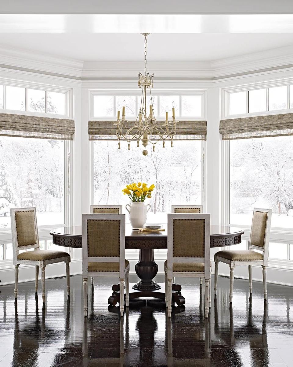 White window shades surround a formal dining table and chandelier